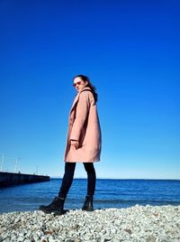Full length of young woman standing at beach against clear blue sky