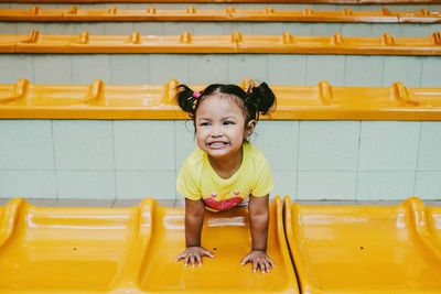 High angle view of cheerful girl leaning on yellow retaining wall