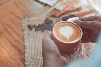 Heart-shaped latte art coffee in red glass on sackcloth and decorated with cinnamon. 