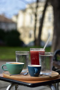 Cappuccino, macchiato, raspberry lemonade and two water glasses on a wooden tray, in a public park