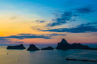 Silhouette rocks in sea against sky during sunset