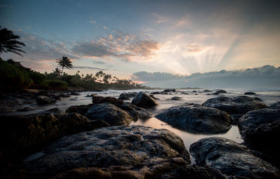 View of rocks at beach against sky during sunset