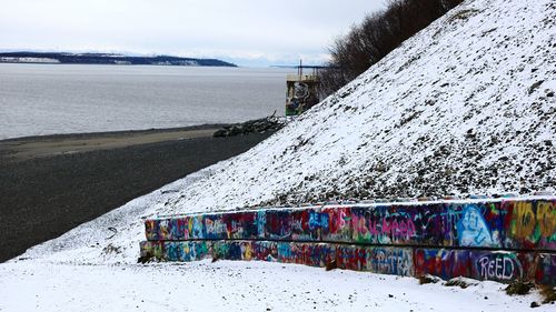 Snow covered land by sea against sky