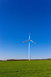 Windmill on field against clear blue sky