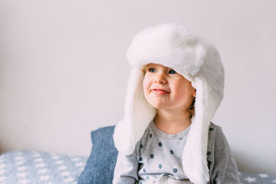 Cute child y on the bed in cozy adult clothes and a hat with earflaps.