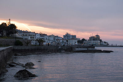 Buildings by sea against sky during sunset