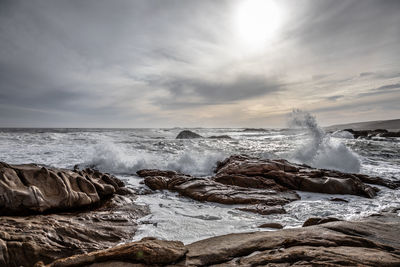 Sea waves splashing on rocks against sky