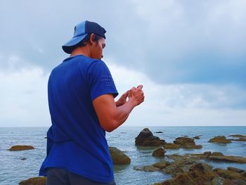 Man standing on rock at beach against sky