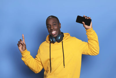 Portrait of smiling man holding mobile phone while standing against blue background