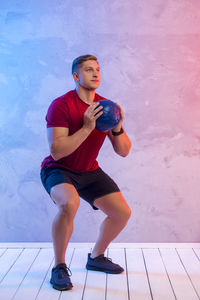 Full length of young man exercising against illuminated wall