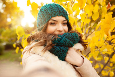 Portrait of beautiful young woman in warm clothing against autumn tree