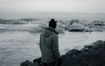 Rear view of woman standing on rock by sea