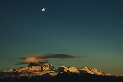 Lenticular cloud over snow covered mountains against sky at morning