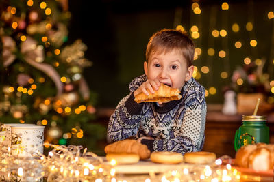 Portrait of boy on table at illuminated christmas tree
