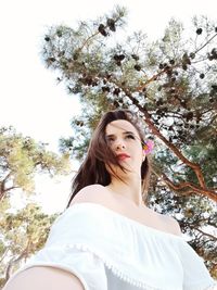 Low angle view of young woman standing against tree