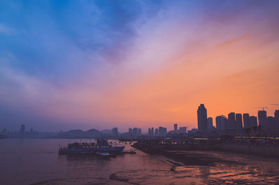 Silhouette buildings in city against sky at sunset