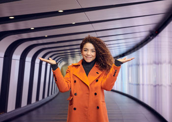 Portrait of young woman gesturing while standing in corridor