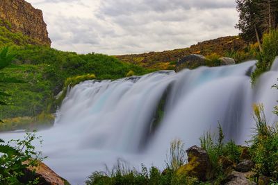 Scenic view of waterfall in forest against sky