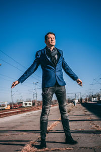 Man standing on railroad station platform against blue sky