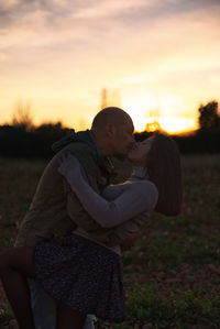 Couple kisses in a natural landscape at sunset.
