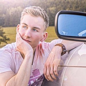 Close-up of handsome young man sitting by car