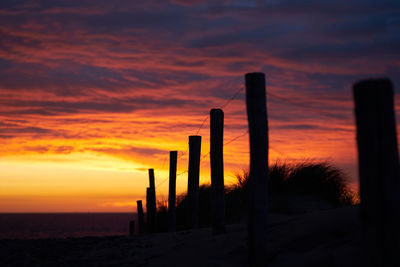 Silhouette wooden posts on field against sky during sunset