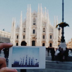 Cropped hand of woman holding photograph against historic buildings