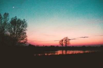 Silhouette trees by lake against sky during sunset