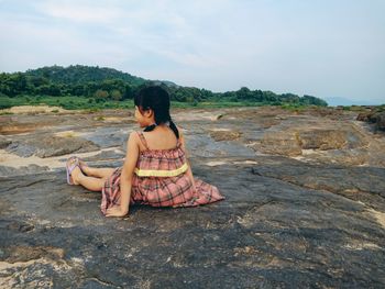 Rear view of girl sitting on rock against sky