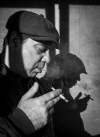 Adult man smoking a cigarette and his shadow on the wall