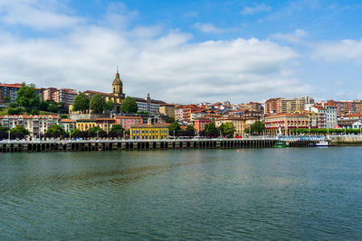 Buildings by river against cloudy sky