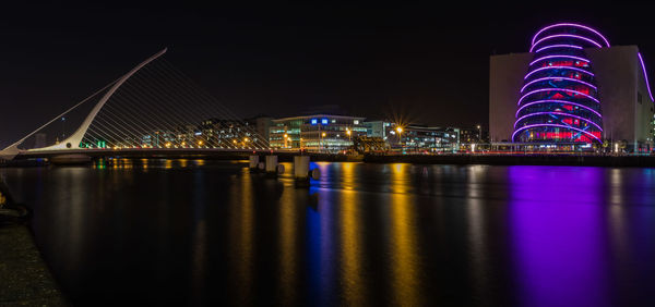 Illuminated samuel beckett bridge and buildings in city at night