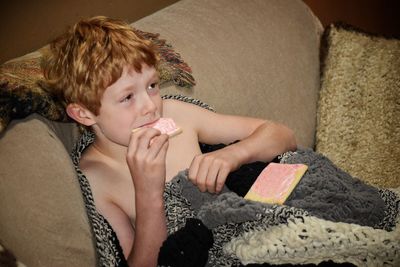 High angle view of shirtless boy eating jam bread in knitted blanket