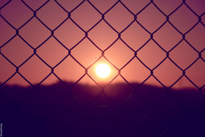 Close-up of silhouette chainlink fence against sky during sunset