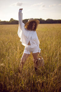 Fashion portrait of a curly-haired woman in white clothes and in a wicker hat and with a basket