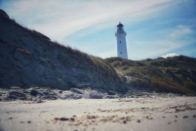 Lighthouse on beach by buildings against sky