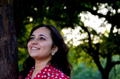 Portrait of smiling young woman against tree trunk