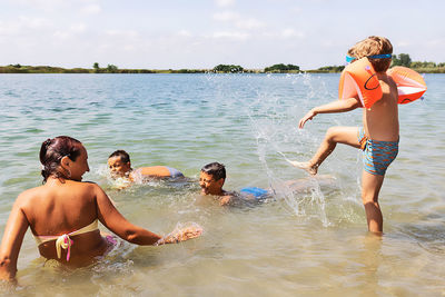 Playful kids and their mother having fun in water during summer day.