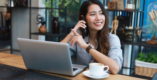 Young woman using phone while sitting on table