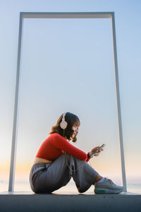 Woman sitting on mobile phone against clear sky