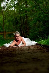 Portrait of bride lying on dirt road in forest