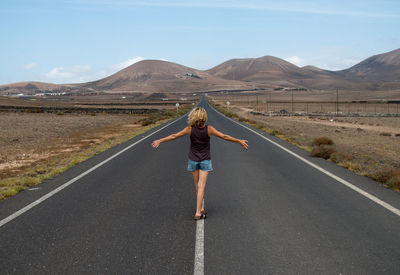 Rear view of woman with arms outstretched walking on country road