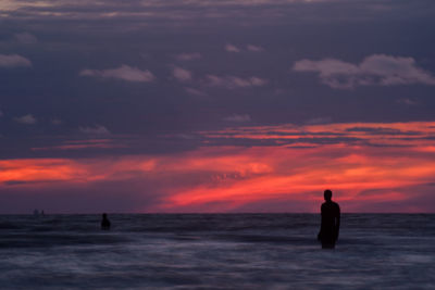 Silhouette another place statue at crosby beach in sea against sky during sunset