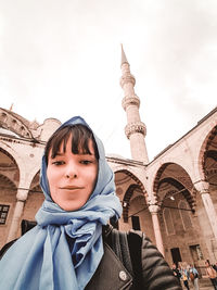 Portrait of young woman standing against mosque