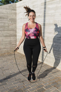 Sportswoman smiling while skipping by wall during sunny day