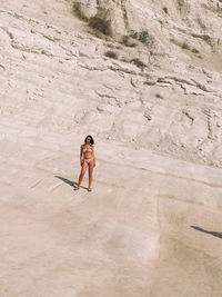Woman wearing bikini standing by rock formation