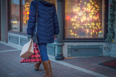 Woman with shopping bags walking on sidewalk in city at night