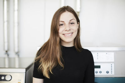 Portrait of smiling young woman with long brown hair standing at laundromat