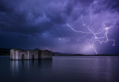 Old ruins in lake against lightning at night
