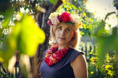 Portrait of young woman wearing floral necklace and wreath in yard